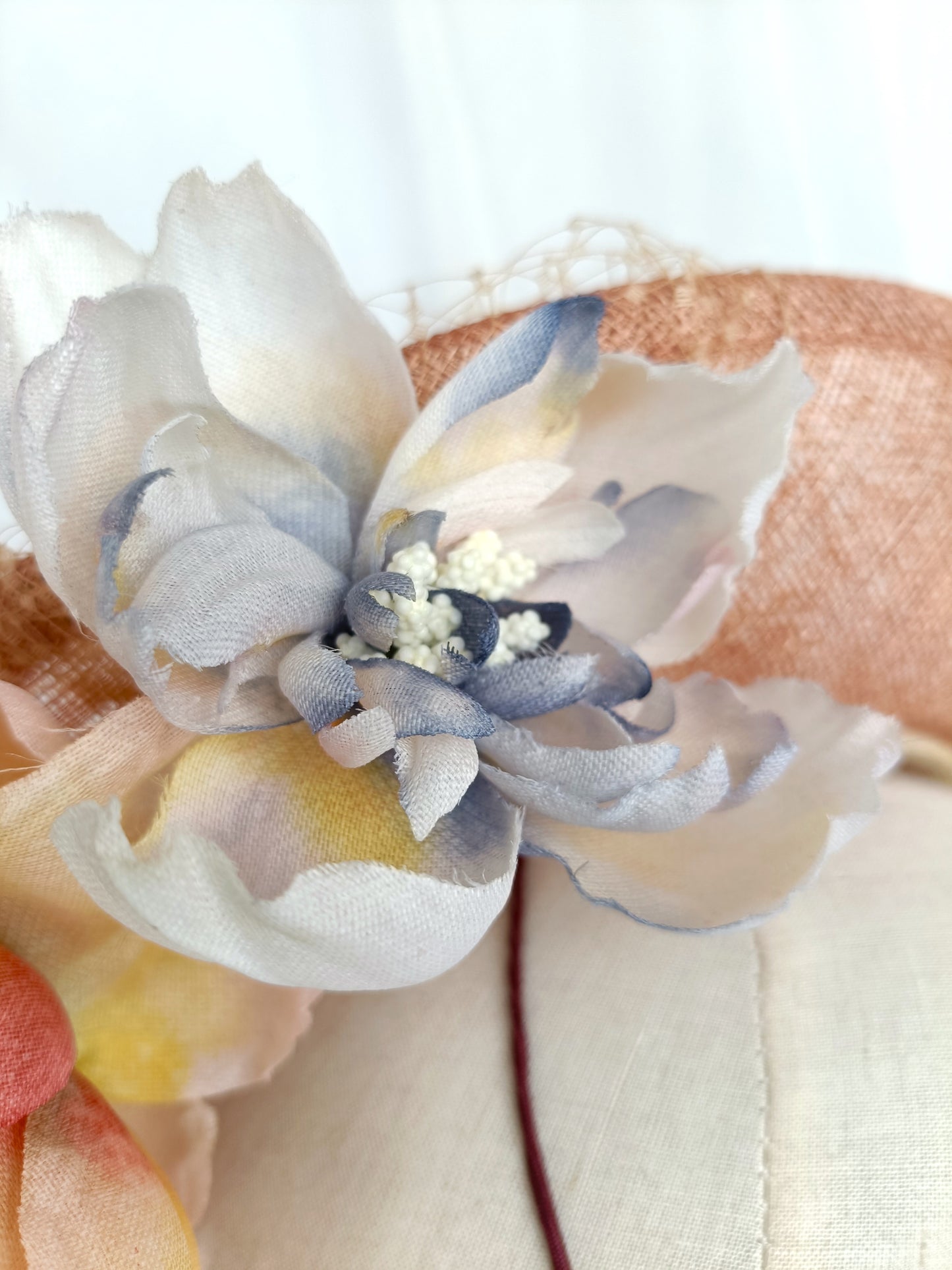 Tocado pamela de invitada en sinamay snaranjado, flores de seda azules y amarillas, con velo decorativo, elegante y colorido para boda.a