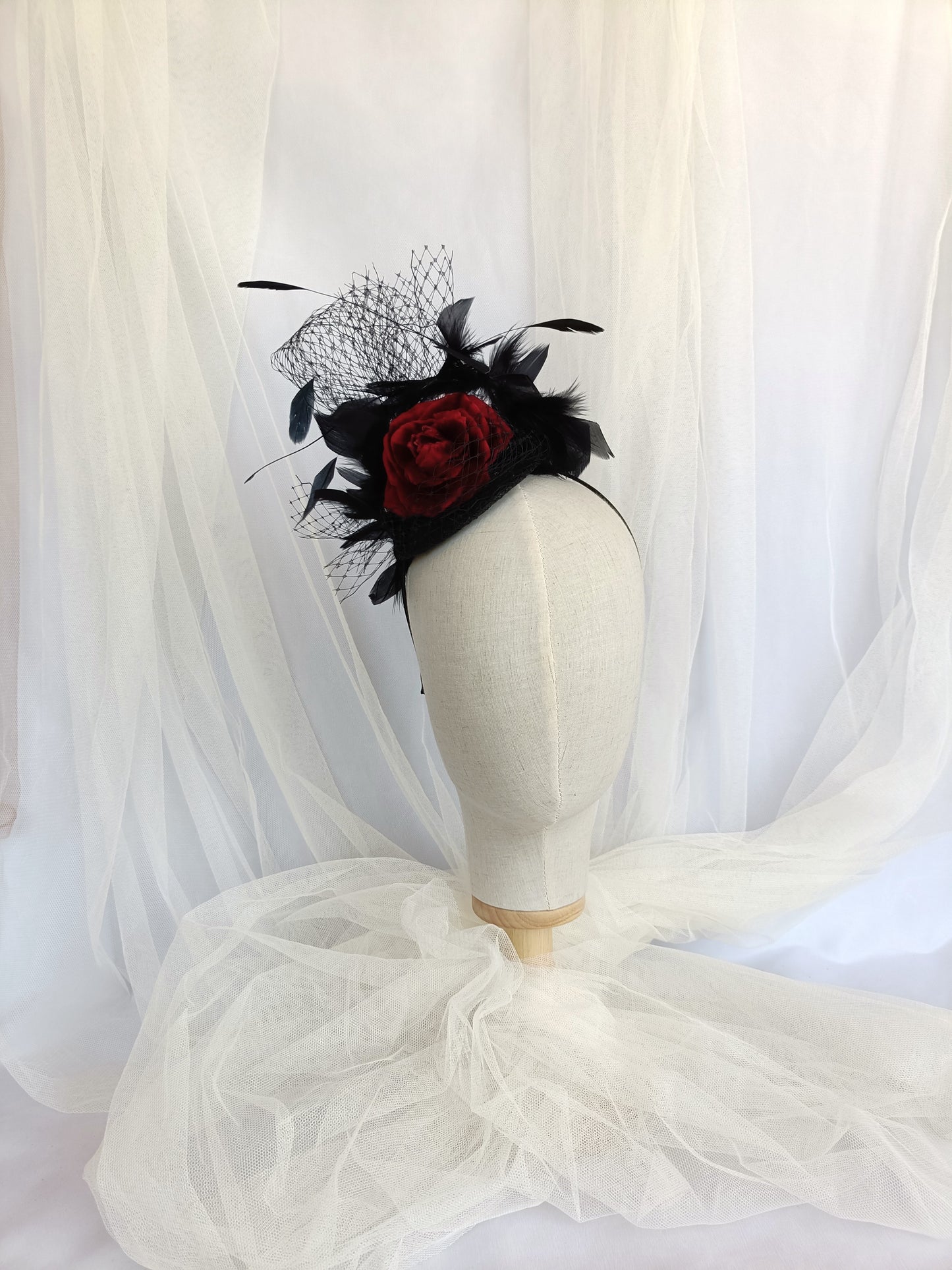 Tocado negro con flor de terciopelo rojo, plumas y velo decorativo, estilo elegante y vintage para invitada de boda.
