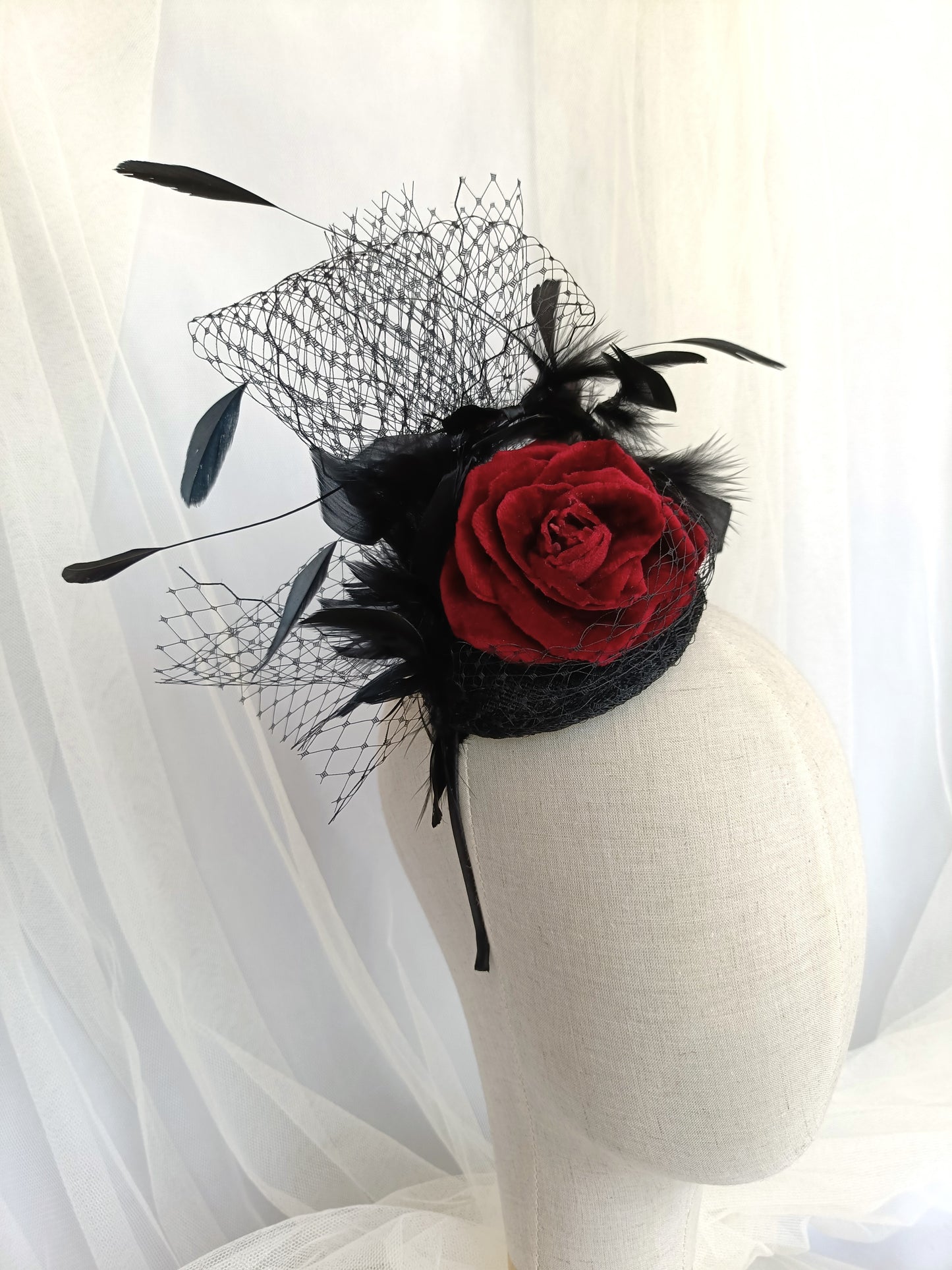 Tocado negro con flor de terciopelo rojo, plumas y velo decorativo, estilo elegante y vintage para invitada de boda.