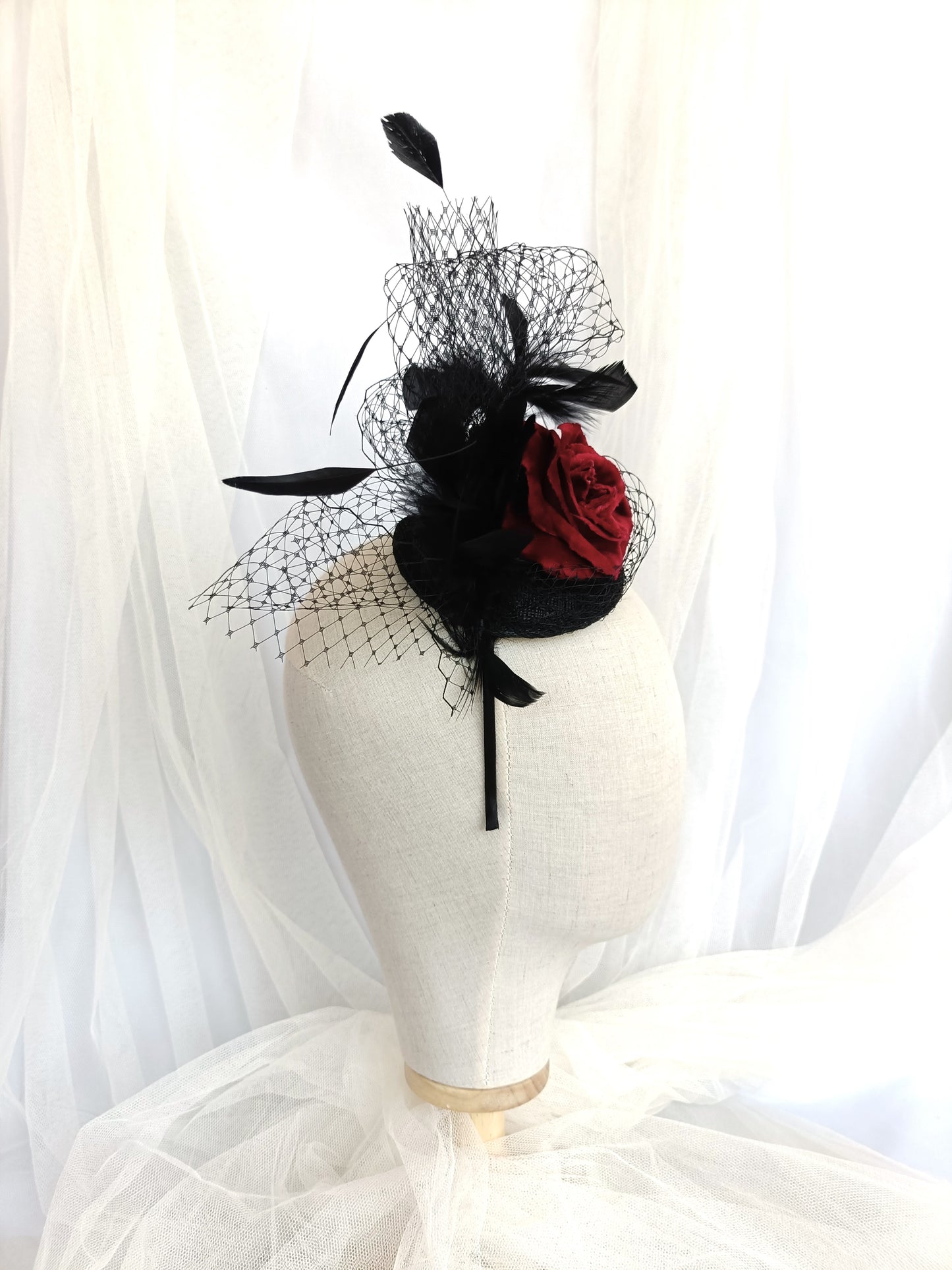 Tocado negro con flor de terciopelo rojo, plumas y velo decorativo, estilo elegante y vintage para invitada de boda.