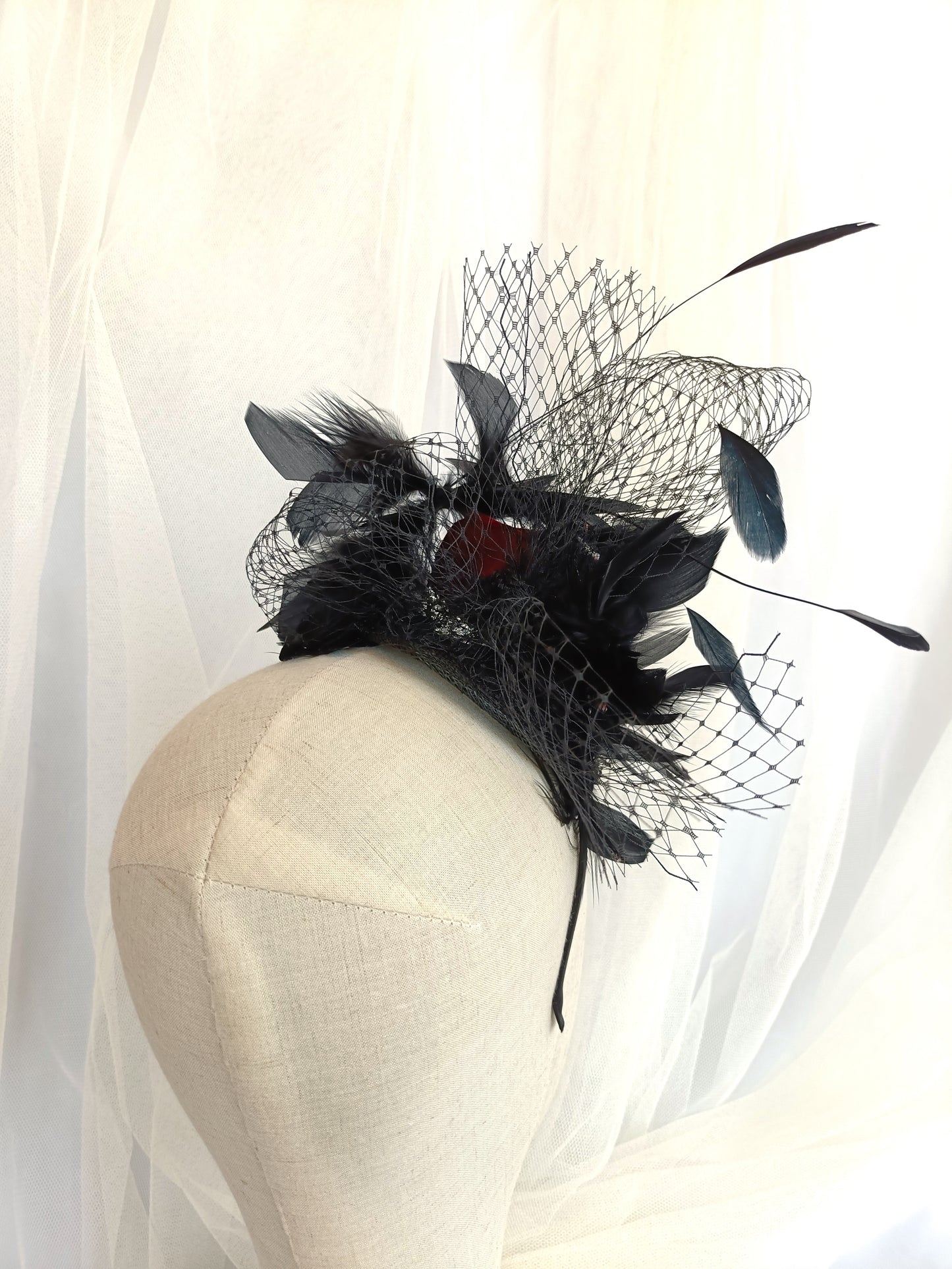 Tocado negro con flor de terciopelo rojo, plumas y velo decorativo, estilo elegante y vintage para invitada de boda.