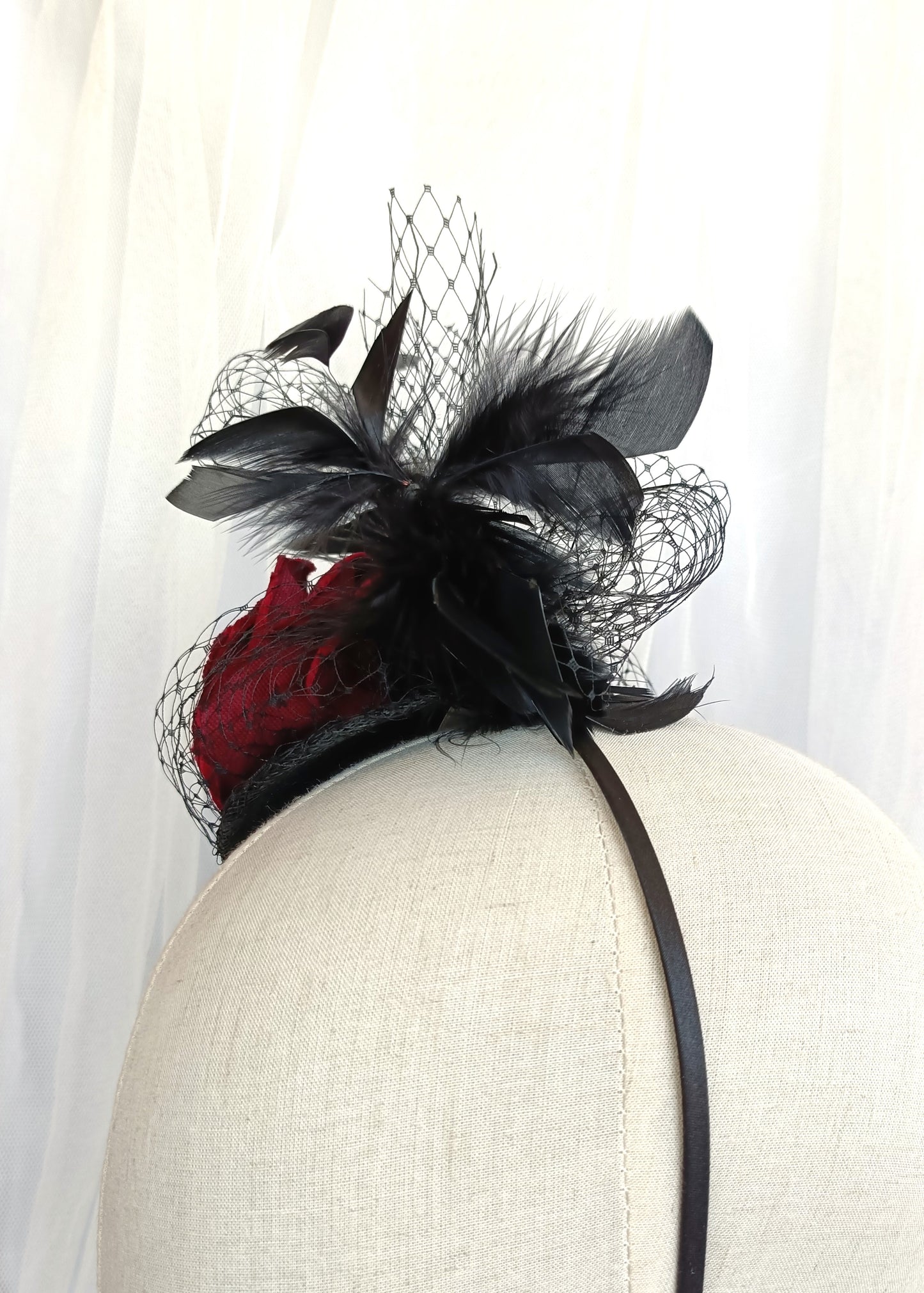 Tocado negro con flor de terciopelo rojo, plumas y velo decorativo, estilo elegante y vintage para invitada de boda.