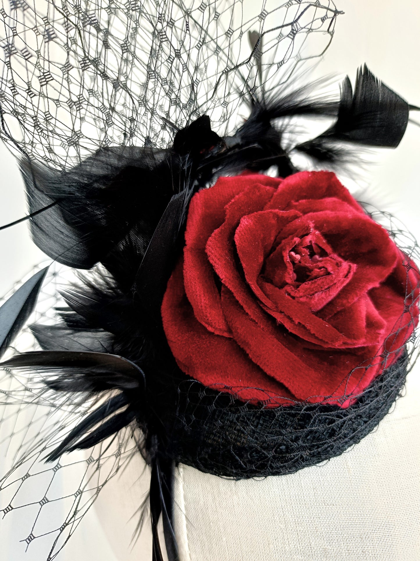 Tocado negro con flor de terciopelo rojo, plumas y velo decorativo, estilo elegante y vintage para invitada de boda.