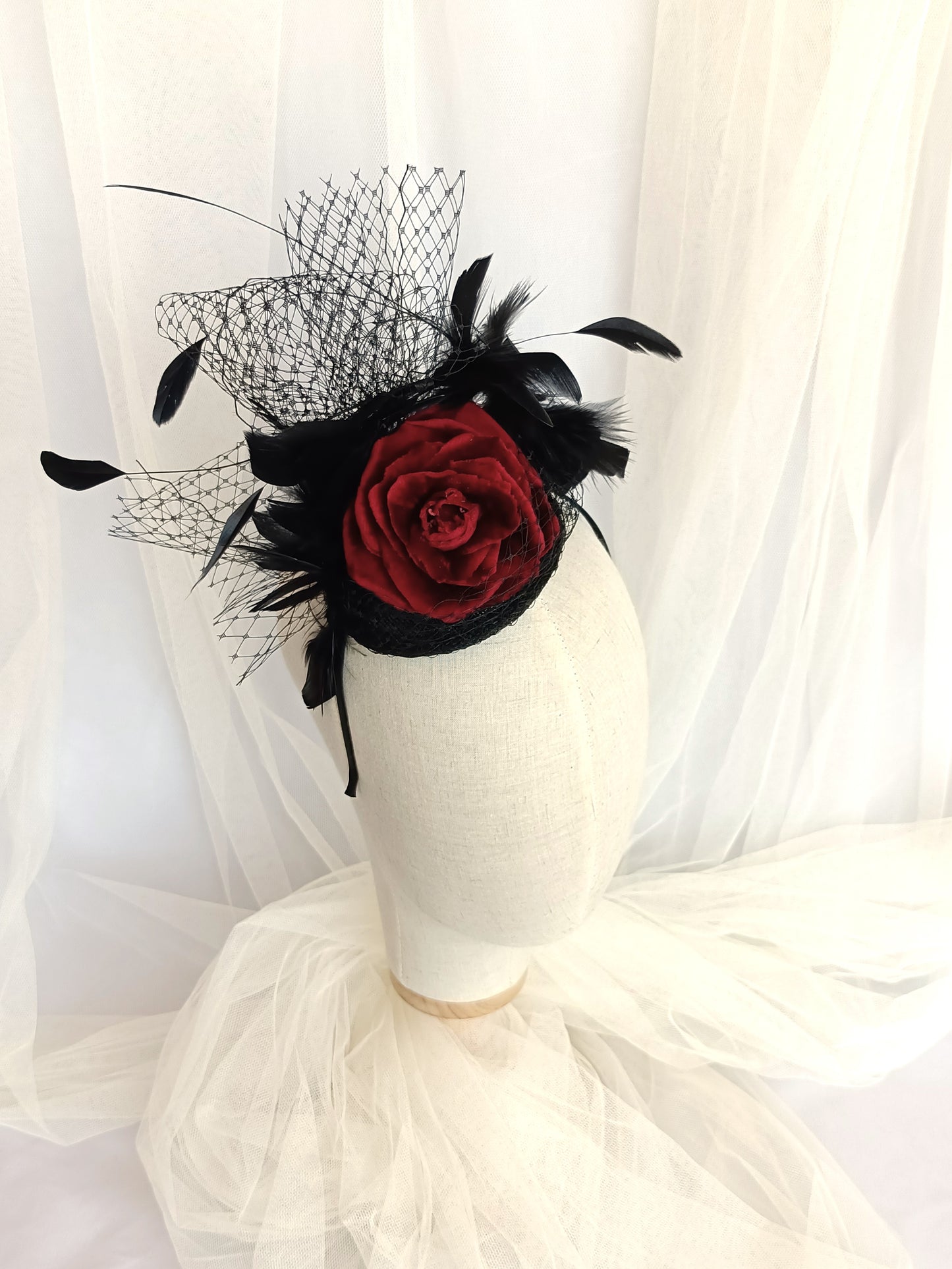 Tocado negro con flor de terciopelo rojo, plumas y velo decorativo, estilo elegante y vintage para invitada de boda.