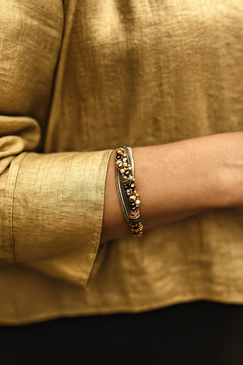 Pulsera de hilos de lino y cuentas en tonos dorados con cadenita decorativa.
