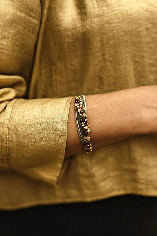 Pulsera de hilos de lino y cuentas en tonos dorados con cadenita decorativa.