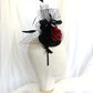 Tocado negro con flor de terciopelo rojo, plumas y velo decorativo, estilo elegante y vintage para invitada de boda.