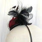 Tocado negro con flor de terciopelo rojo, plumas y velo decorativo, estilo elegante y vintage para invitada de boda.