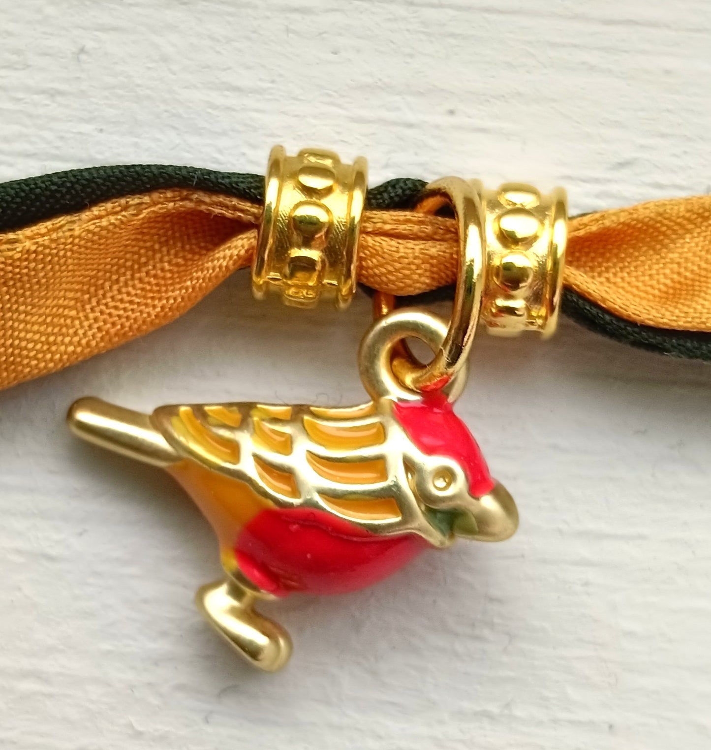 Pulsera de seda verde y mostaza con pajarita esmaltada