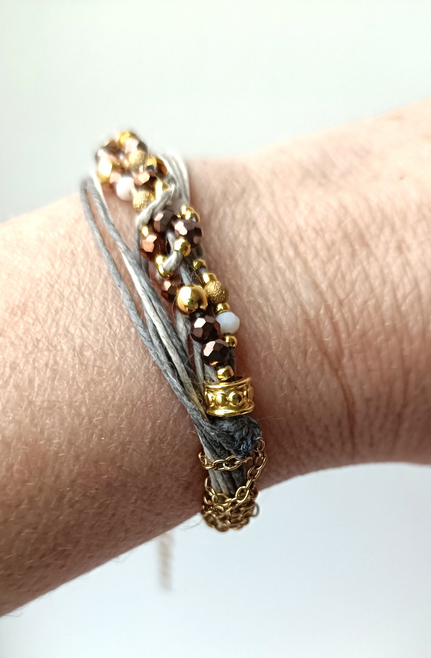 Pulsera de hilos de lino y cuentas en tonos dorados con cadenita decorativa.