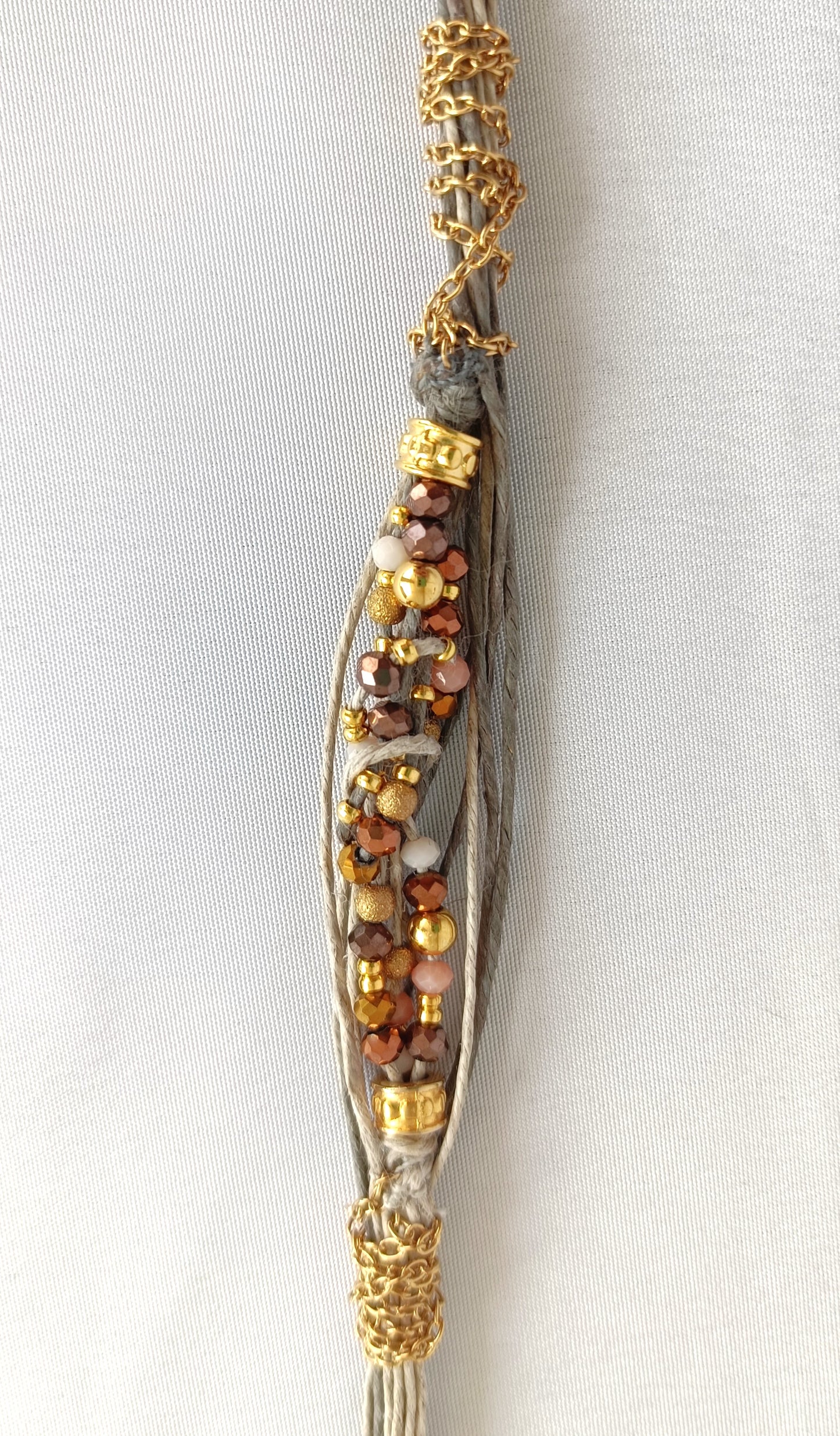 Pulsera de hilos de lino y cuentas en tonos dorados con cadenita decorativa.