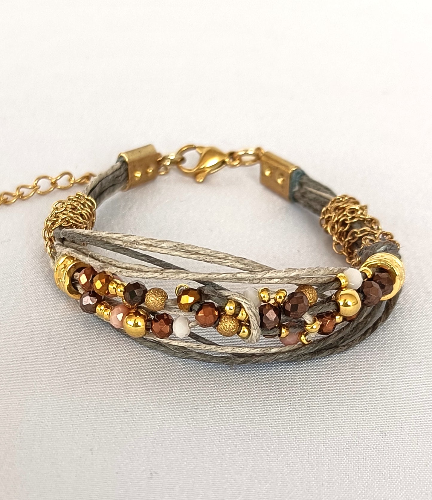 Pulsera de hilos de lino y cuentas en tonos dorados con cadenita decorativa.