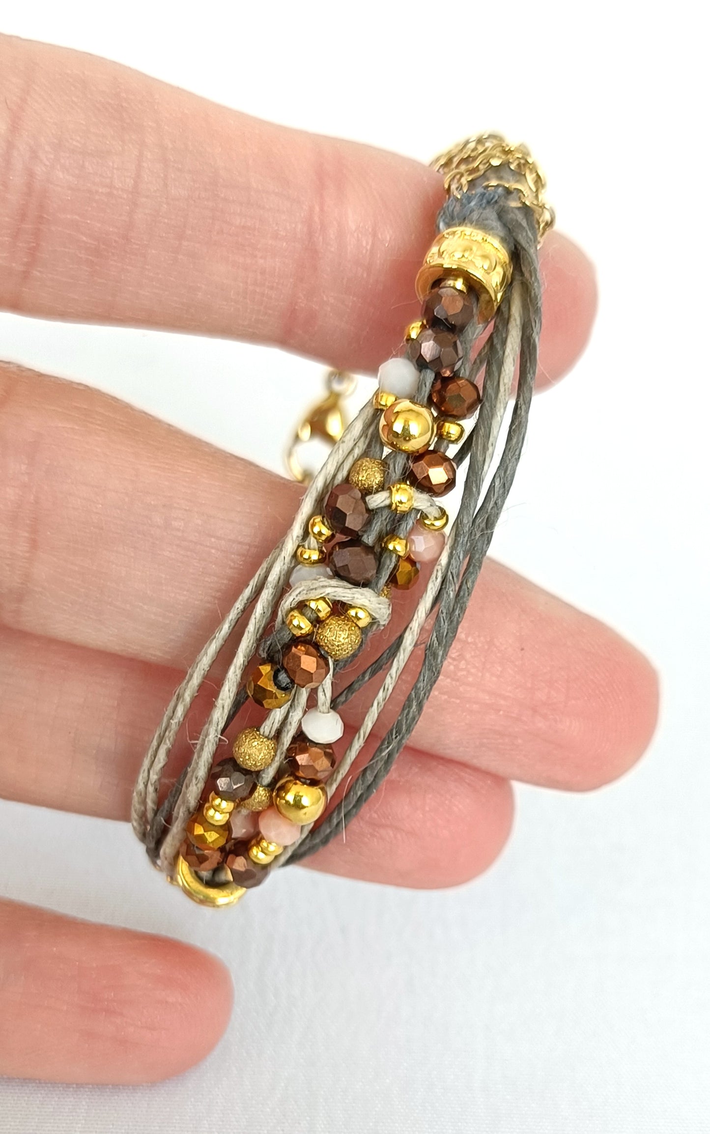 Pulsera de hilos de lino y cuentas en tonos dorados con cadenita decorativa.