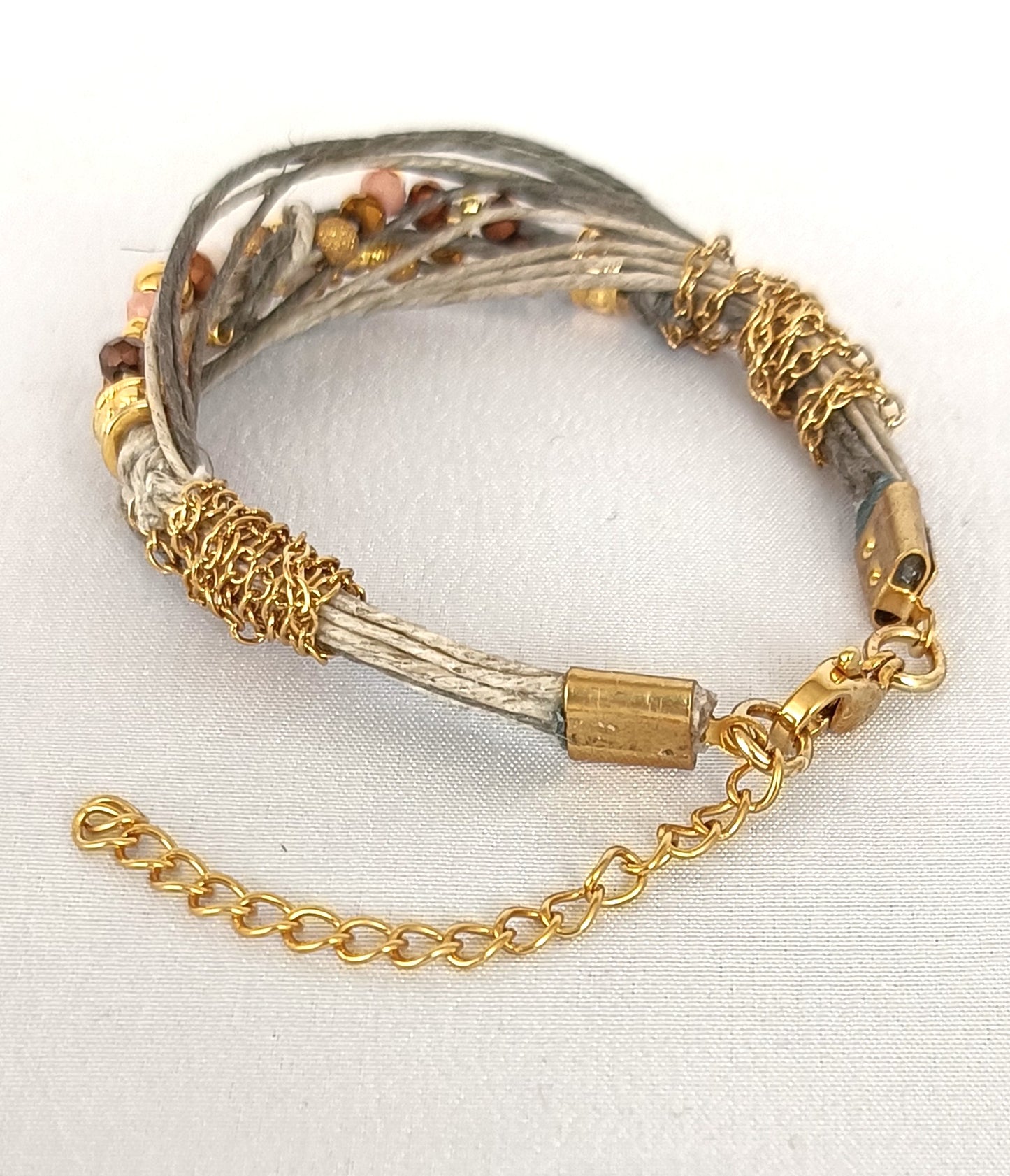 Pulsera de hilos de lino y cuentas en tonos dorados con cadenita decorativa.