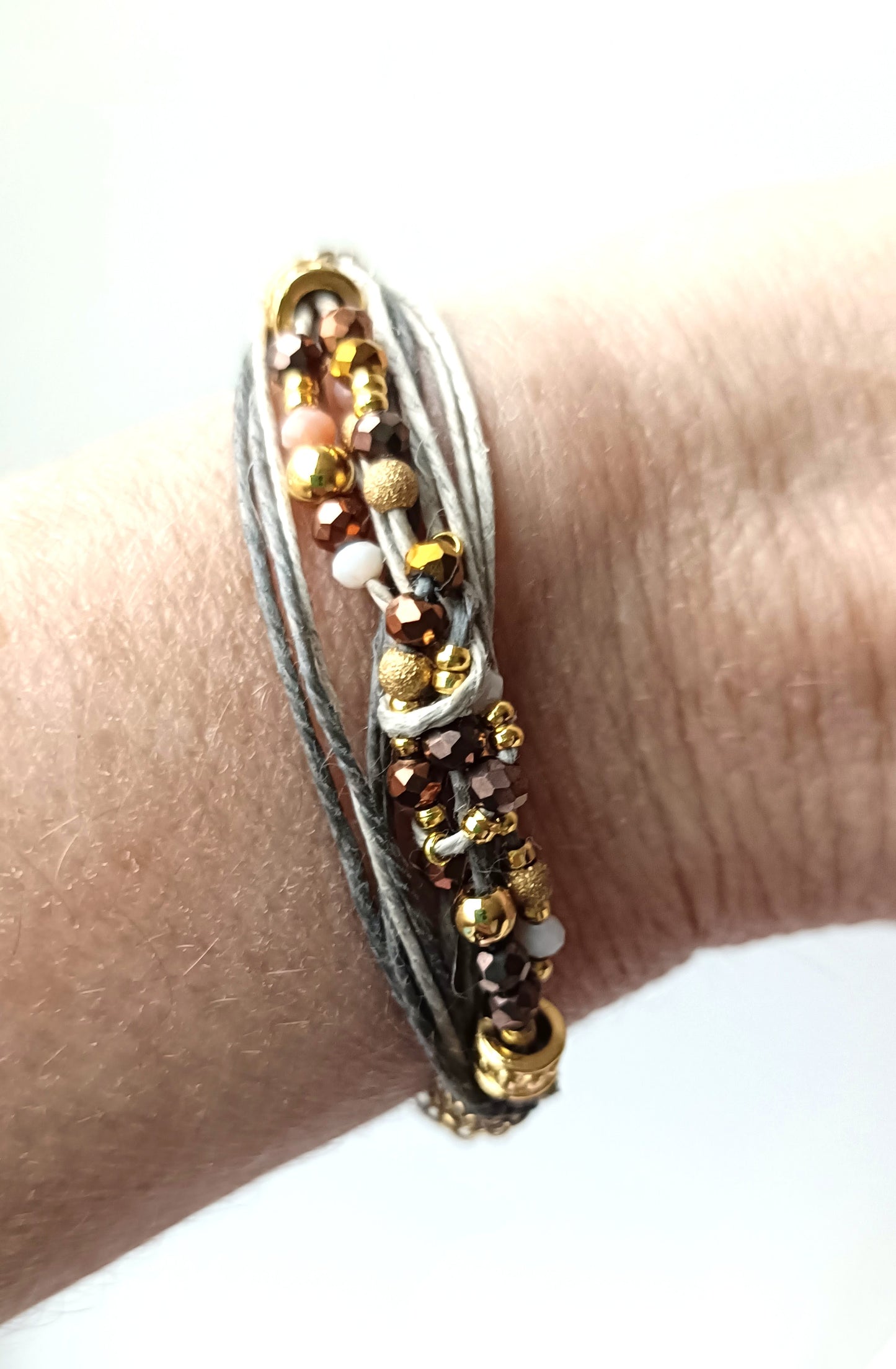 Pulsera de hilos de lino y cuentas en tonos dorados con cadenita decorativa.