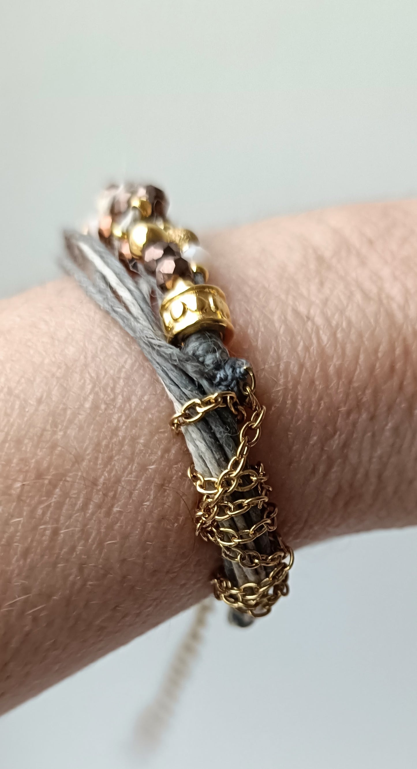 Pulsera de hilos de lino y cuentas en tonos dorados con cadenita decorativa.