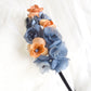 Diadema de flores de seda en azul y naranja, diseño elegante y romántico para invitada de boda o evento especial.